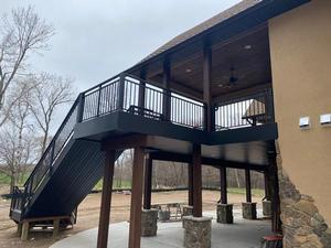 Black steel deck frame over a stone patio with a covered lower level